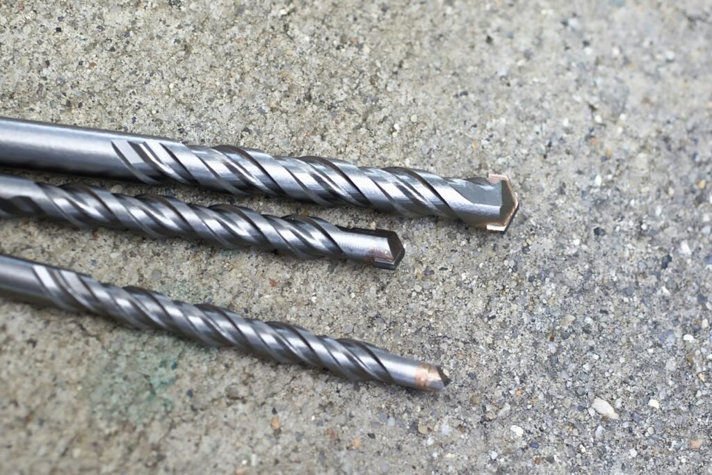 Three metal drill bits on a concrete surface